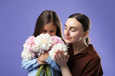 Photo of Mother and her daughter with bouquet of beautiful peonies on purple background