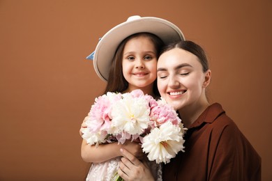 Photo of Mother and her daughter with bouquet of beautiful peonies on brown background, space for text