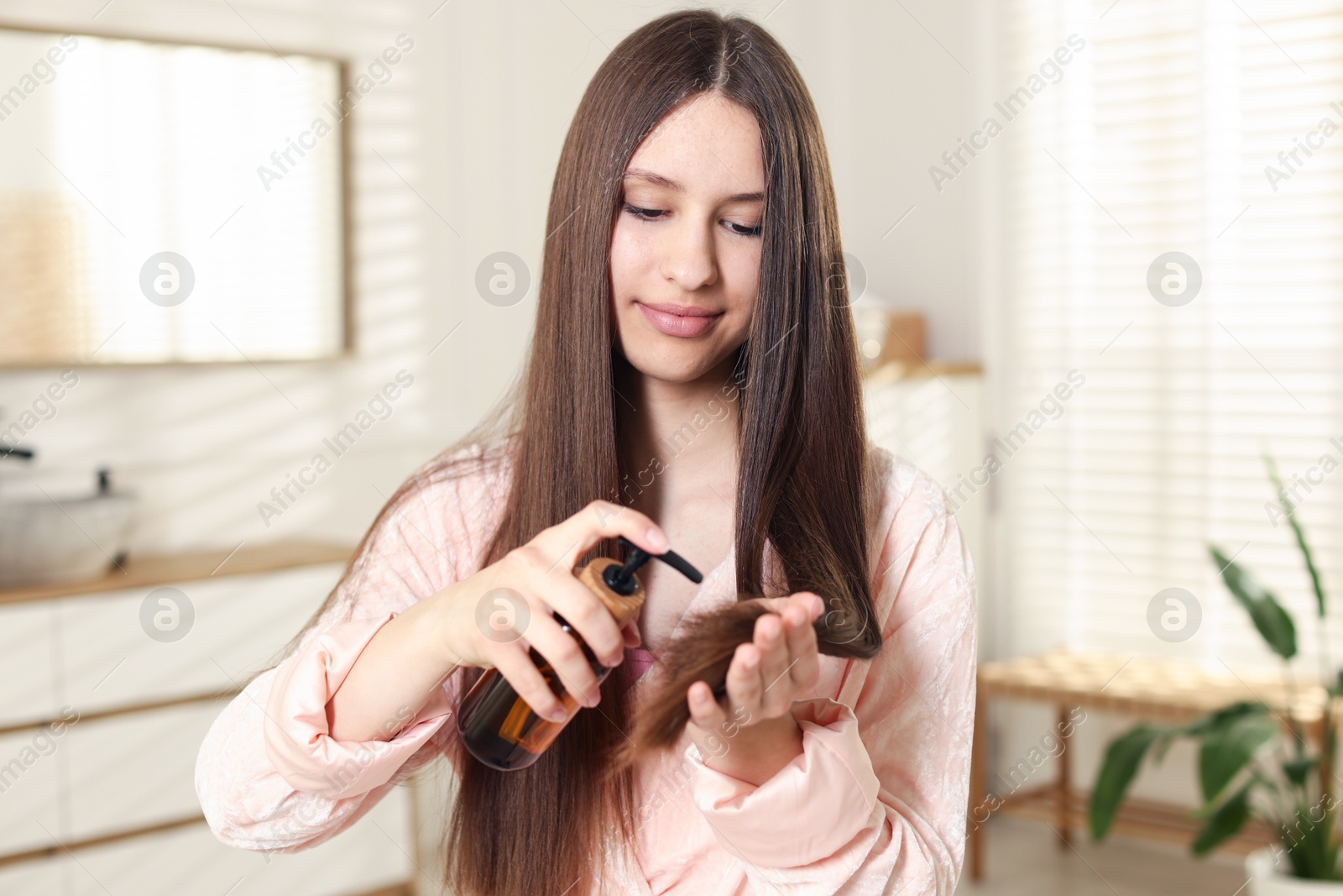 Teenage girl applying cosmetic product onto her hair at home Photo of Teenage girl applying cosmetic product onto her hair at home