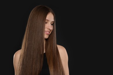 Photo of Smiling teenage girl with healthy long hair on black background. Space for text