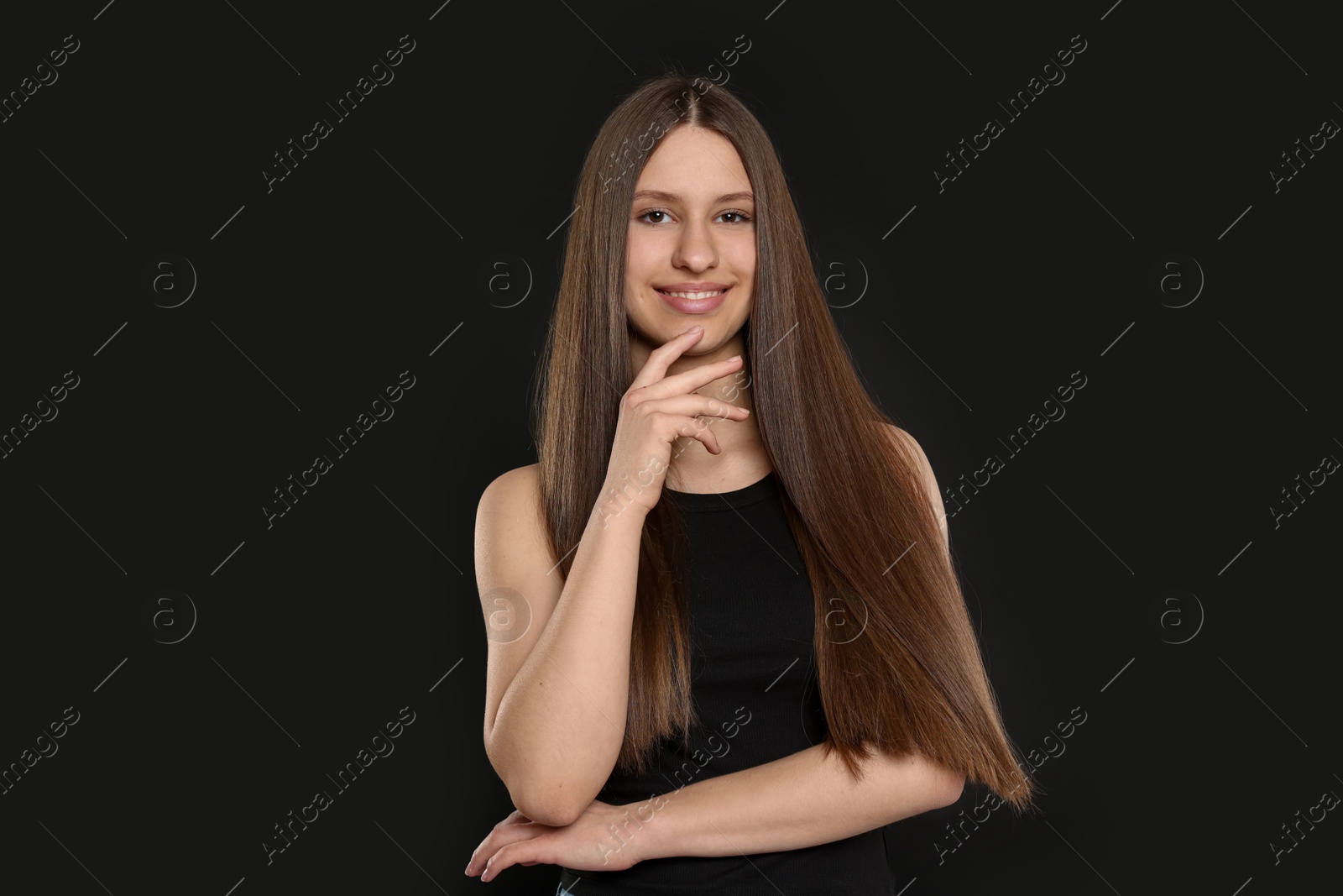 Portrait of smiling teenage girl with healthy long hair on black background Photo of Portrait of smiling teenage girl with healthy long hair on black background