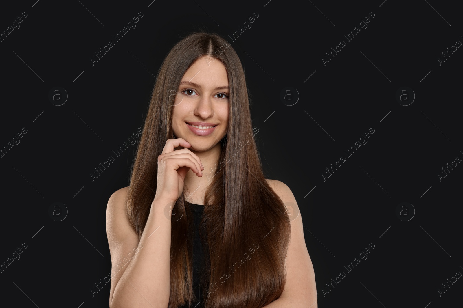 Photo of Portrait of smiling teenage girl with healthy long hair on black background