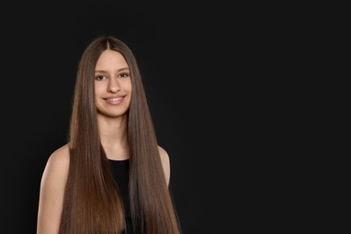 Photo of Smiling teenage girl with healthy long hair on black background. Space for text