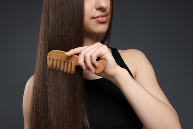 Photo of Teenage girl brushing her healthy long hair on dark grey background, closeup