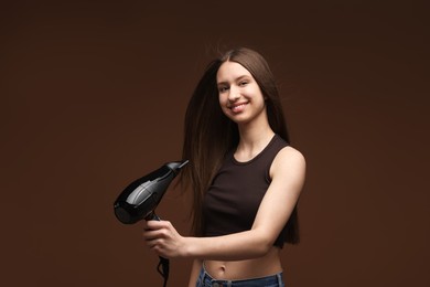Photo of Smiling teenage girl with hair dryer on brown background