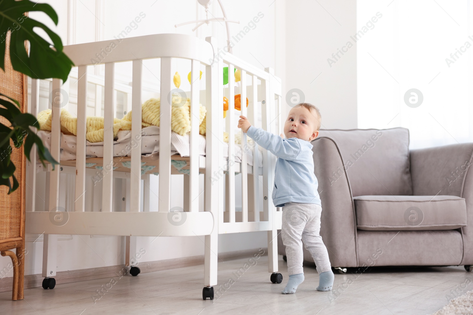 Cute little baby playing near crib in room Photo of Cute little baby playing near crib in room