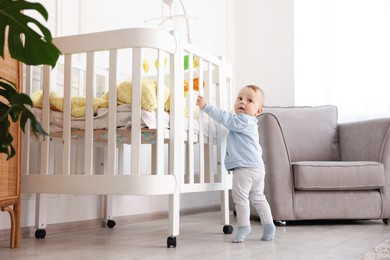 Photo of Cute little baby playing near crib in room