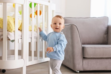 Photo of Cute little baby playing near crib in room