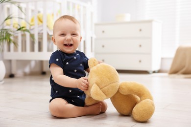 Photo of Cute little baby playing with teddy bear in room