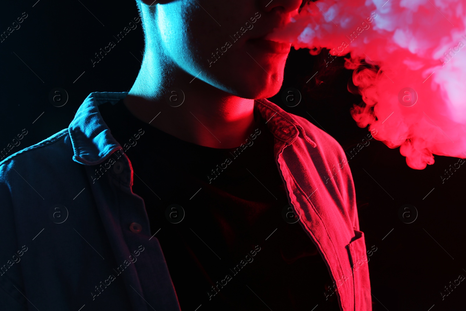 Man using electronic smoking device in neon lights on black background, closeup Photo of Man using electronic smoking device in neon lights on black background, closeup