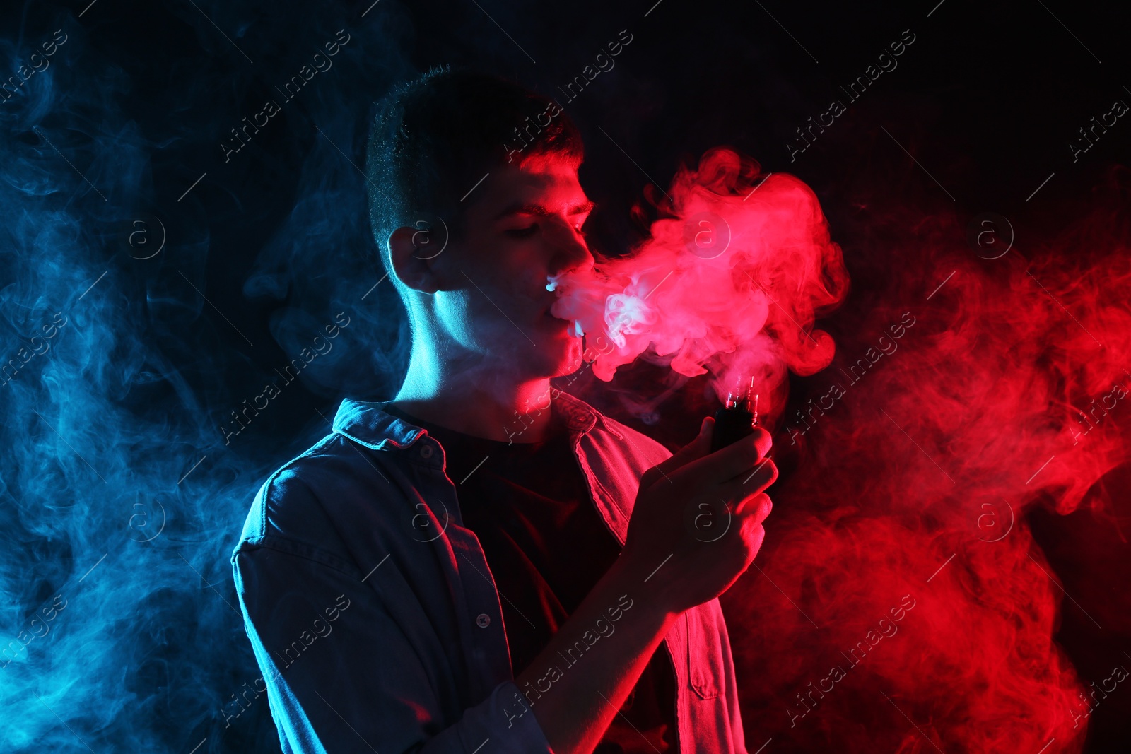 Man using electronic smoking device in neon lights on dark background Photo of Man using electronic smoking device in neon lights on dark background