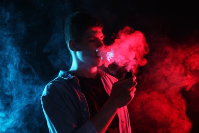 Photo of Man using electronic smoking device in neon lights on dark background