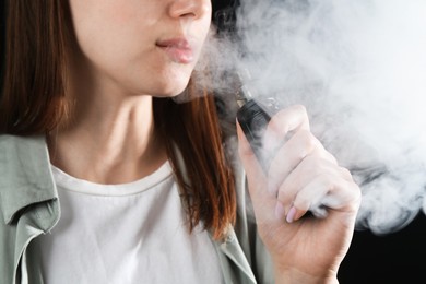 Photo of Woman using electronic smoking device on black background, closeup