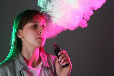 Photo of Woman using electronic smoking device in neon lights on grey background, space for text