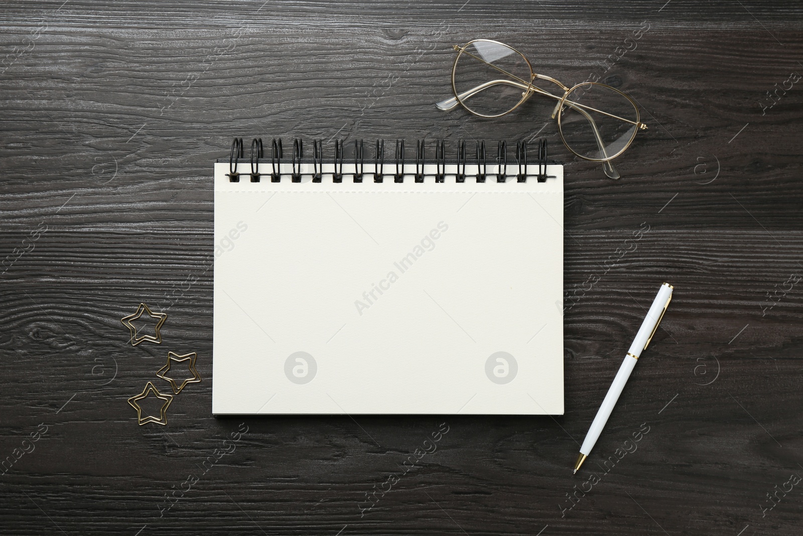 Open blank notebook, glasses, paperclips and pen on black wooden table, flat lay Photo of Open blank notebook, glasses, paperclips and pen on black wooden table, flat lay