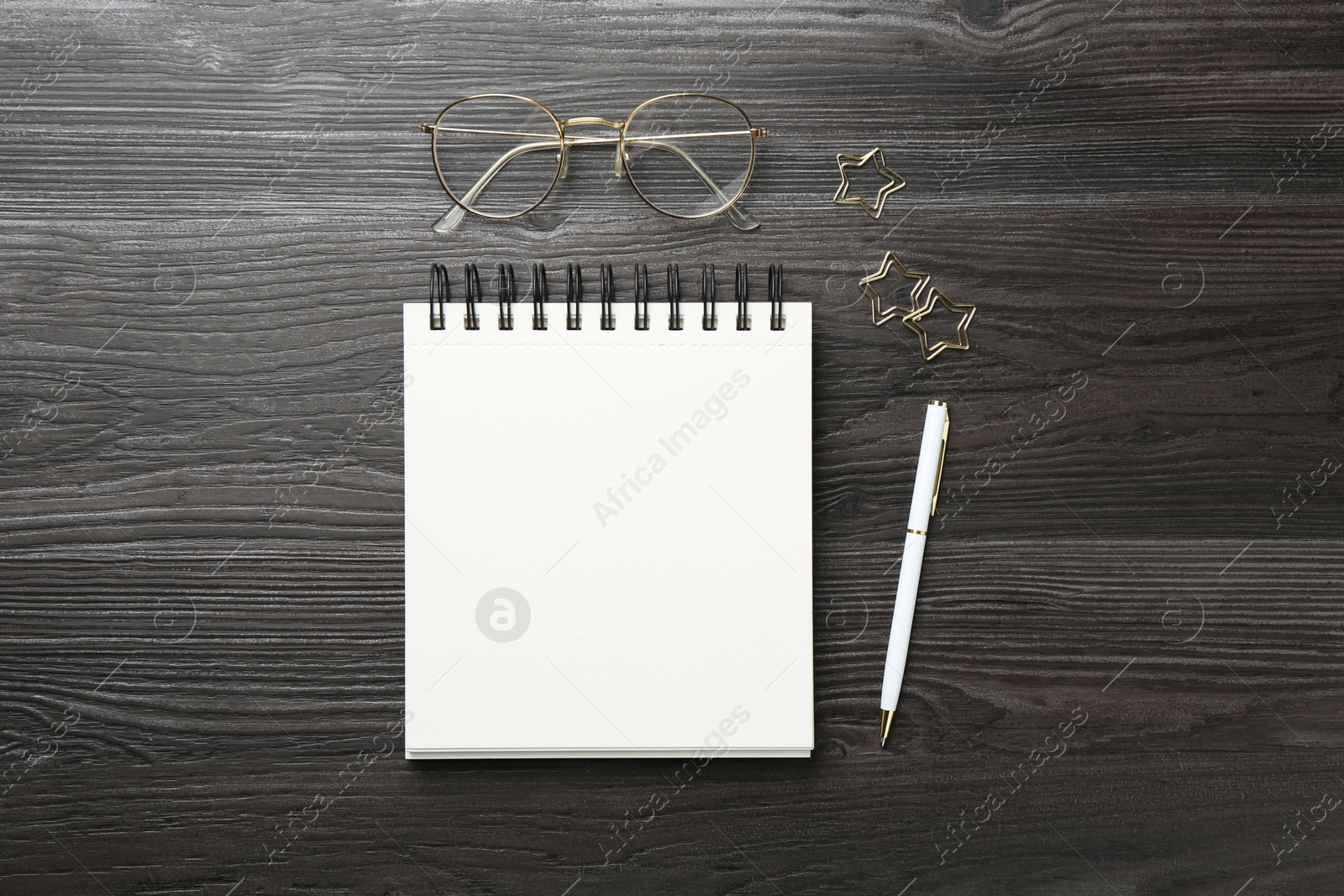 Photo of Open blank notebook, glasses, paperclips and pen on black wooden table, flat lay