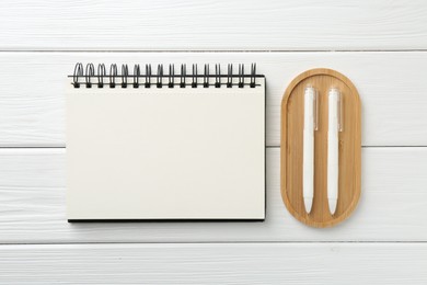 Photo of Open blank notebook and pens on white wooden table, flat lay
