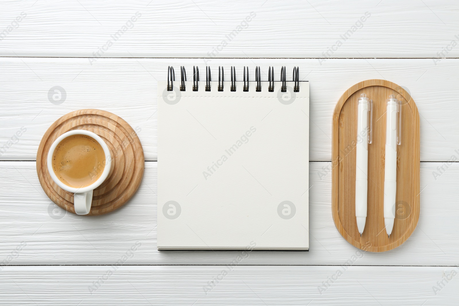 Photo of Open blank notebook, coffee and pens on white wooden table, flat lay