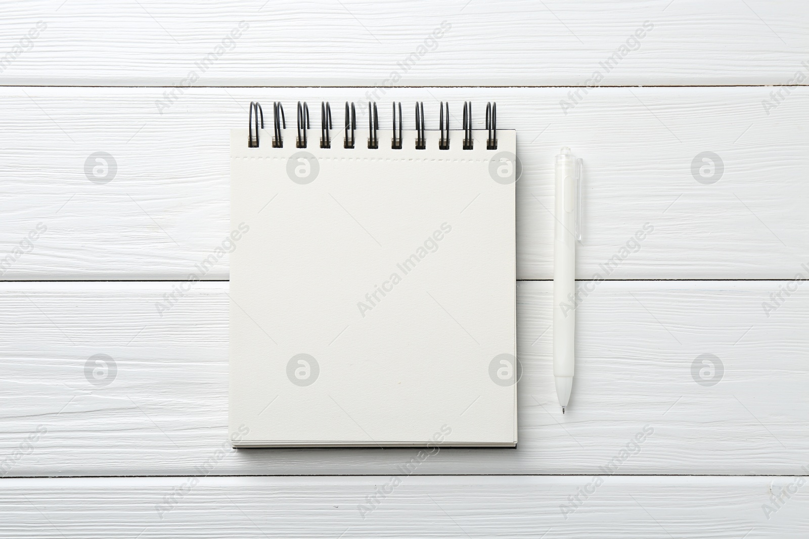 Photo of Open blank notebook and pen on white wooden table, top view
