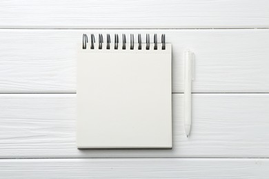 Photo of Open blank notebook and pen on white wooden table, top view