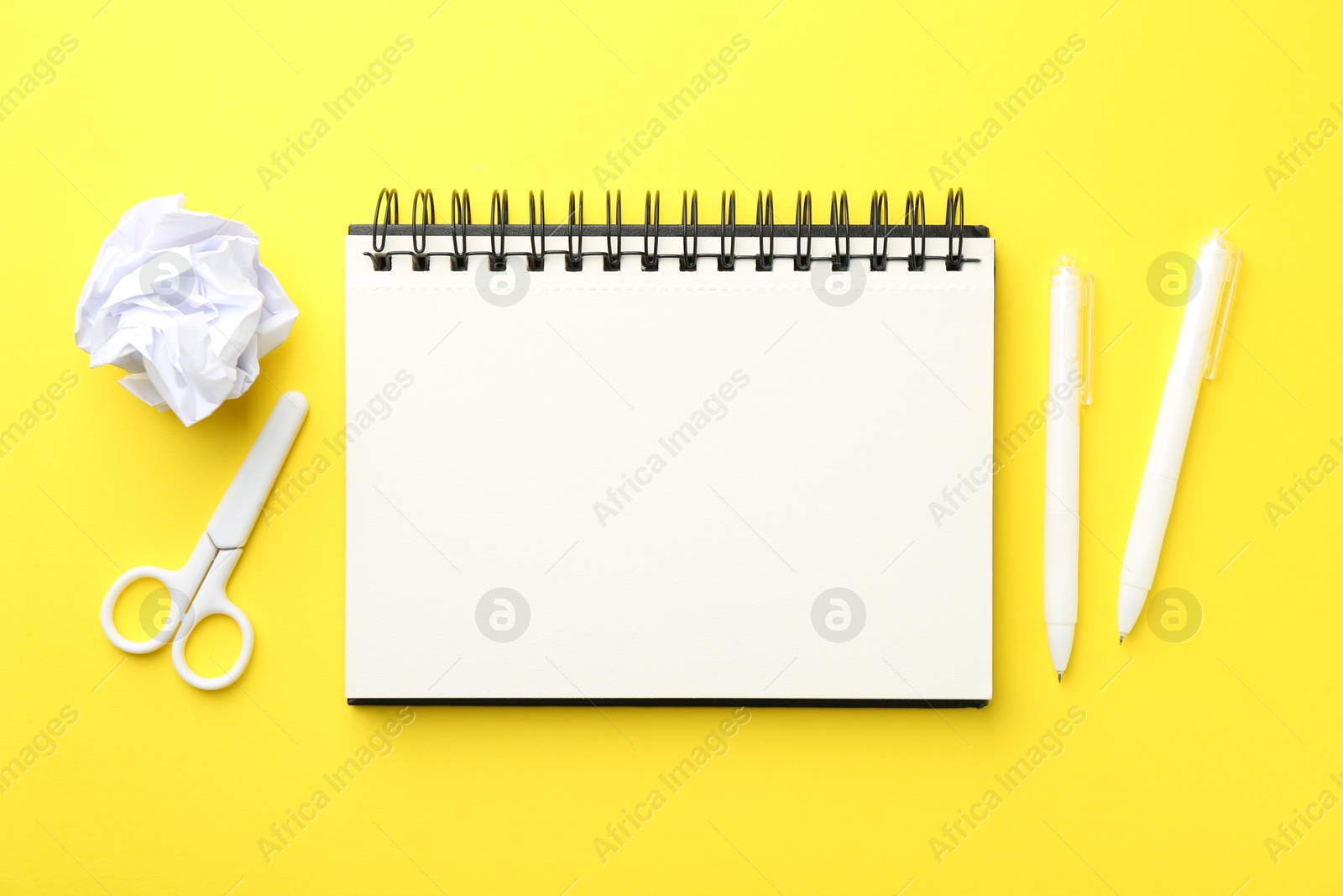 Photo of Open blank notebook, crumpled paper, scissors and pens on yellow background, flat lay
