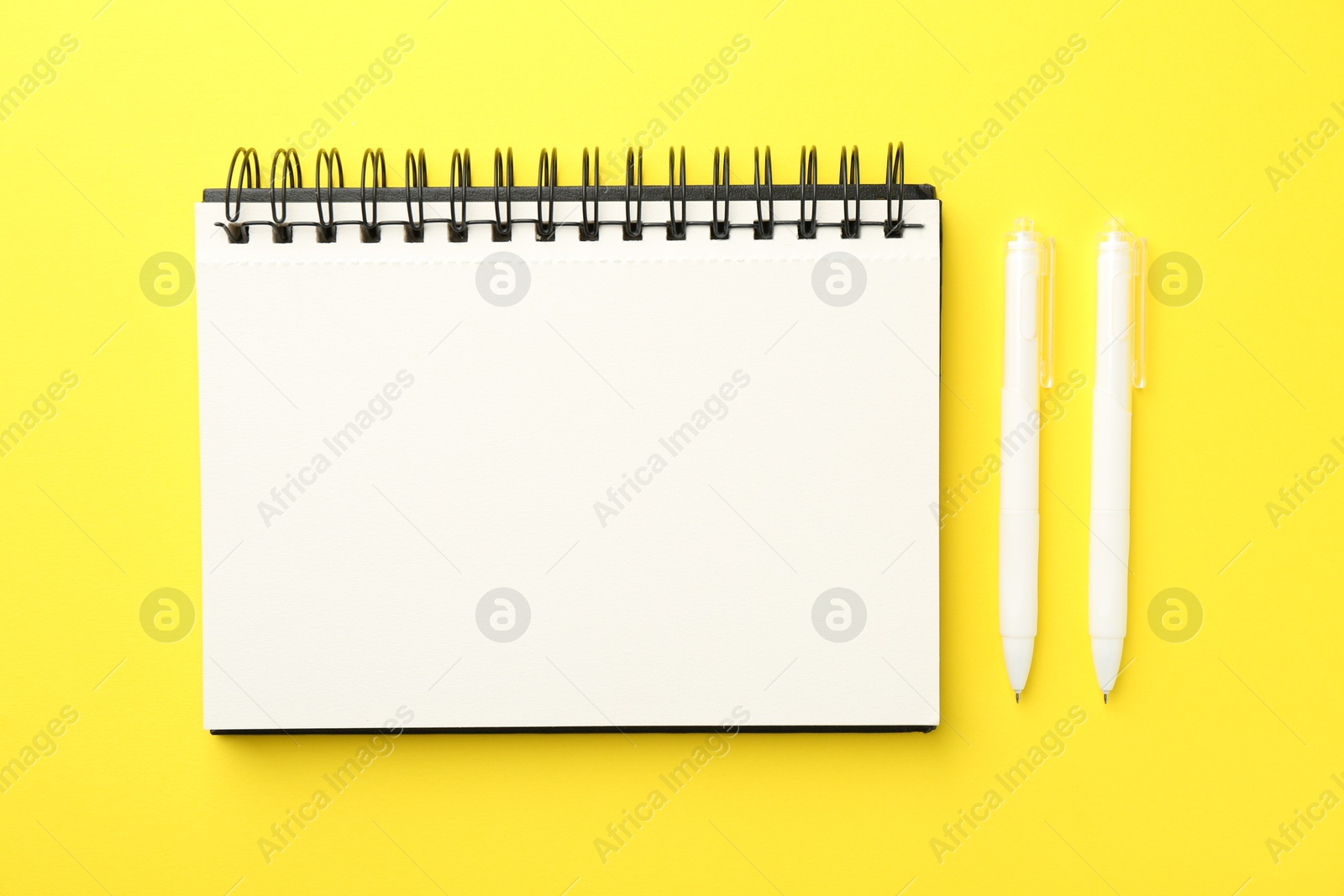 Photo of Open blank notebook and pens on yellow background, flat lay