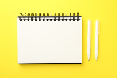 Photo of Open blank notebook and pens on yellow background, flat lay