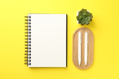 Photo of Open blank notebook, plant and pens on yellow background, flat lay