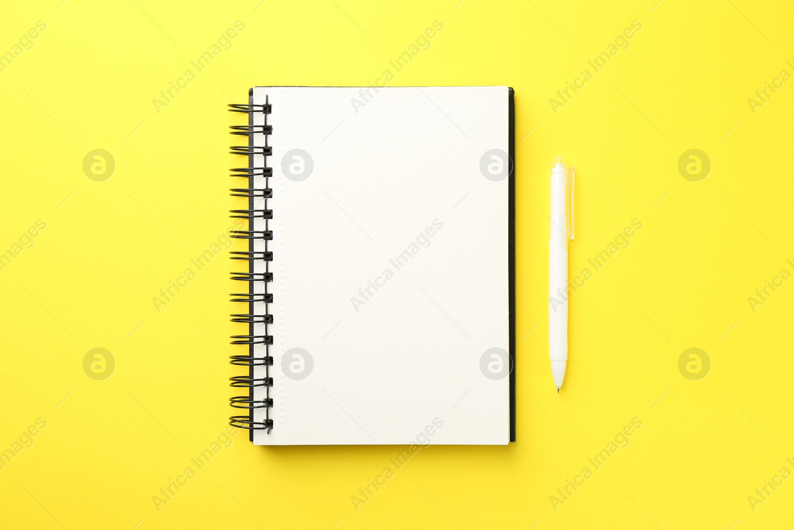 Photo of Open blank notebook and pen on yellow background, top view