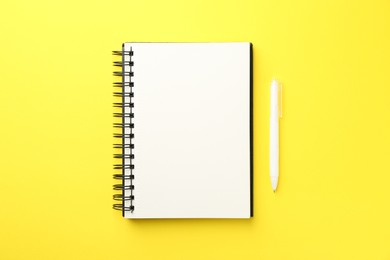 Photo of Open blank notebook and pen on yellow background, top view