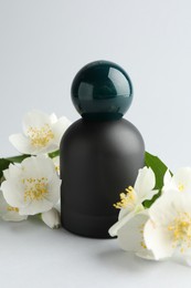 Photo of Bottle of perfume and jasmine flowers on light background, closeup