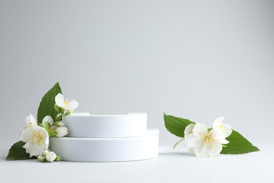 Photo of Beautiful jasmine flowers with leaves on light background. Space for text