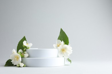 Photo of Beautiful jasmine flowers with leaves on light background. Space for text