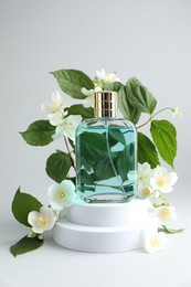 Photo of Bottle of perfume and jasmine flowers on light background