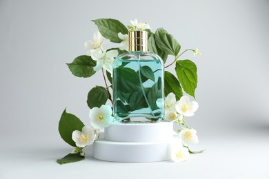 Photo of Bottle of perfume and jasmine flowers on light background