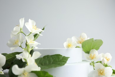 Photo of Beautiful jasmine flowers with leaves on light background, closeup. Space for text