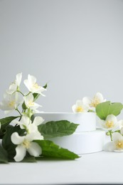 Photo of Beautiful jasmine flowers with leaves on light background, closeup. Space for text