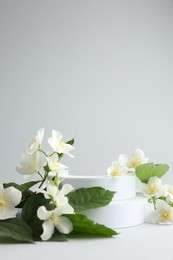 Photo of Beautiful jasmine flowers with leaves on light background. Space for text