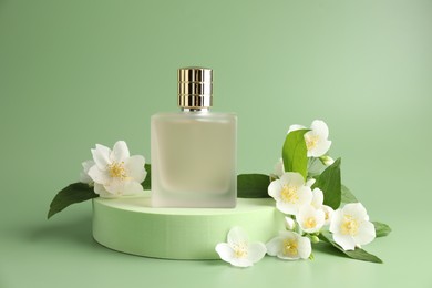 Photo of Bottle of perfume and jasmine flowers on green background