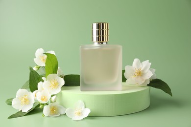 Photo of Bottle of perfume and jasmine flowers on green background
