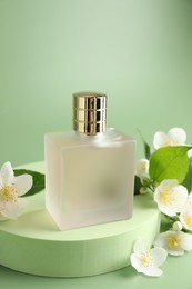 Photo of Bottle of perfume and jasmine flowers on green background, closeup