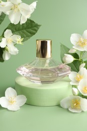 Photo of Bottle of perfume and jasmine flowers on green background, closeup
