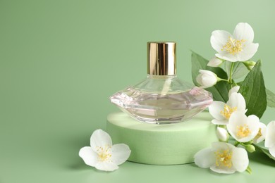 Photo of Bottle of perfume and jasmine flowers on green background, closeup. Space for text