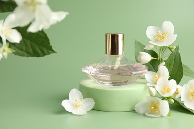 Photo of Bottle of perfume and jasmine flowers on green background, closeup