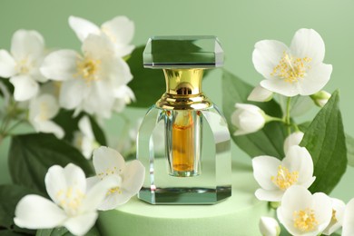 Photo of Bottle of perfume and jasmine flowers on green background, closeup