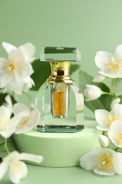 Photo of Bottle of perfume and jasmine flowers on green background, closeup