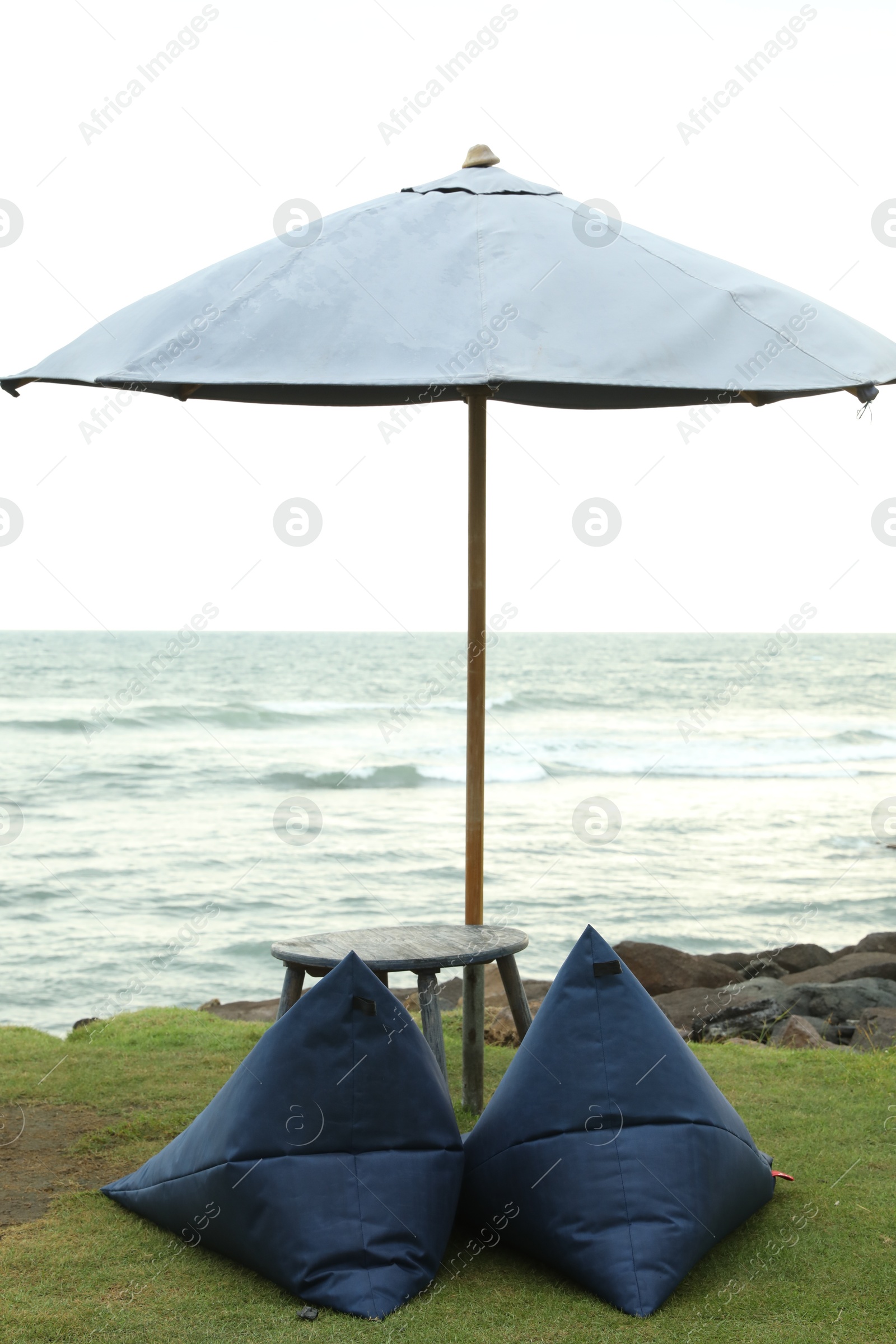 Bean bag chairs, table and umbrella near sea on beautiful beach Photo of Bean bag chairs, table and umbrella near sea on beautiful beach