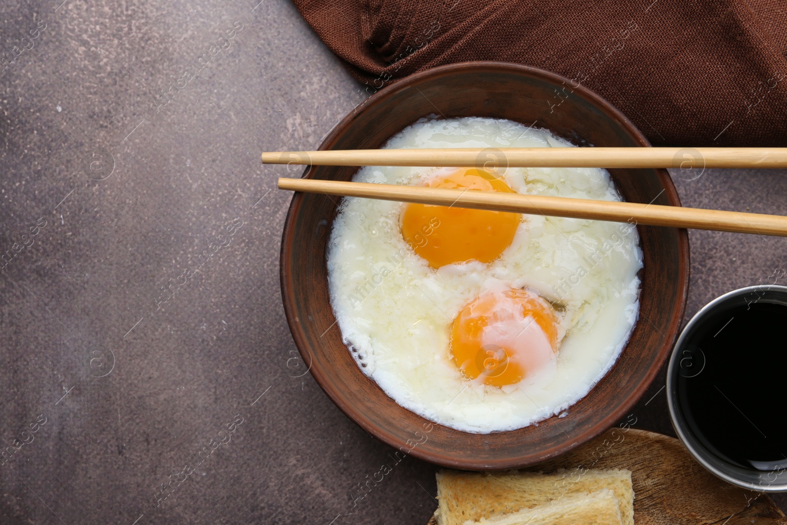 Half-boiled eggs in bowl, chopsticks, soy sauce and toasted bread on brown table, flat lay. Space for text Photo of Half-boiled eggs in bowl, chopsticks, soy sauce and toasted bread on brown table, flat lay. Space for text