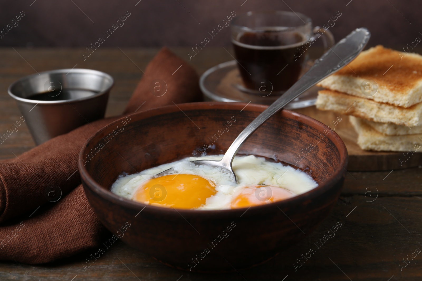 Photo of Half-boiled eggs in bowl, soy sauce and toasted bread on wooden table, closeup