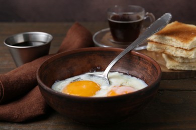 Photo of Half-boiled eggs in bowl, soy sauce and toasted bread on wooden table, closeup